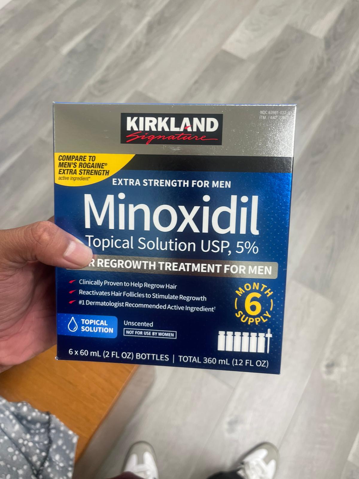 Kirkland Minoxidil topical solution packaging held by a person on a gray surface.