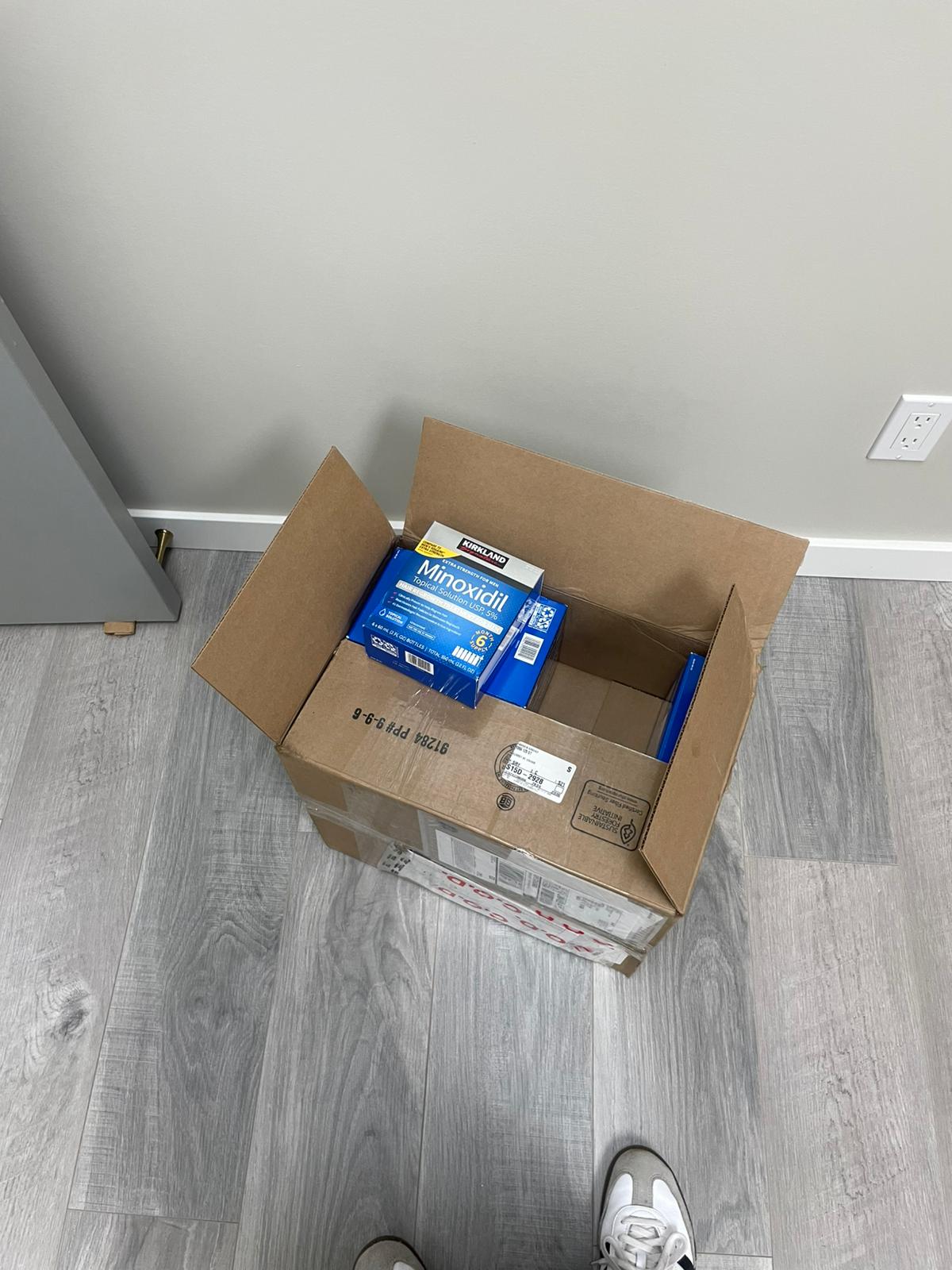 Cardboard box with Maxell batteries on a gray wooden floor.